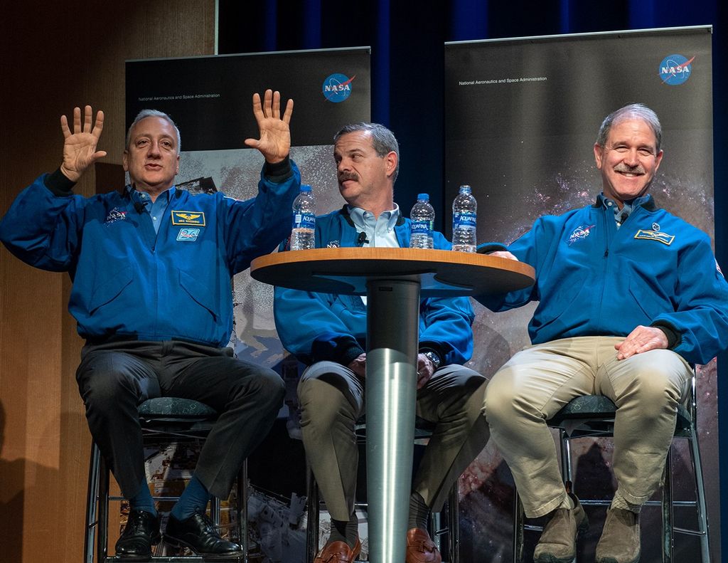Mike Massimino (left) speaks to the audience while using his hands to visualize, while Scott Altman (center) looks at him and John Grunsfeld (right) smiles at the audience