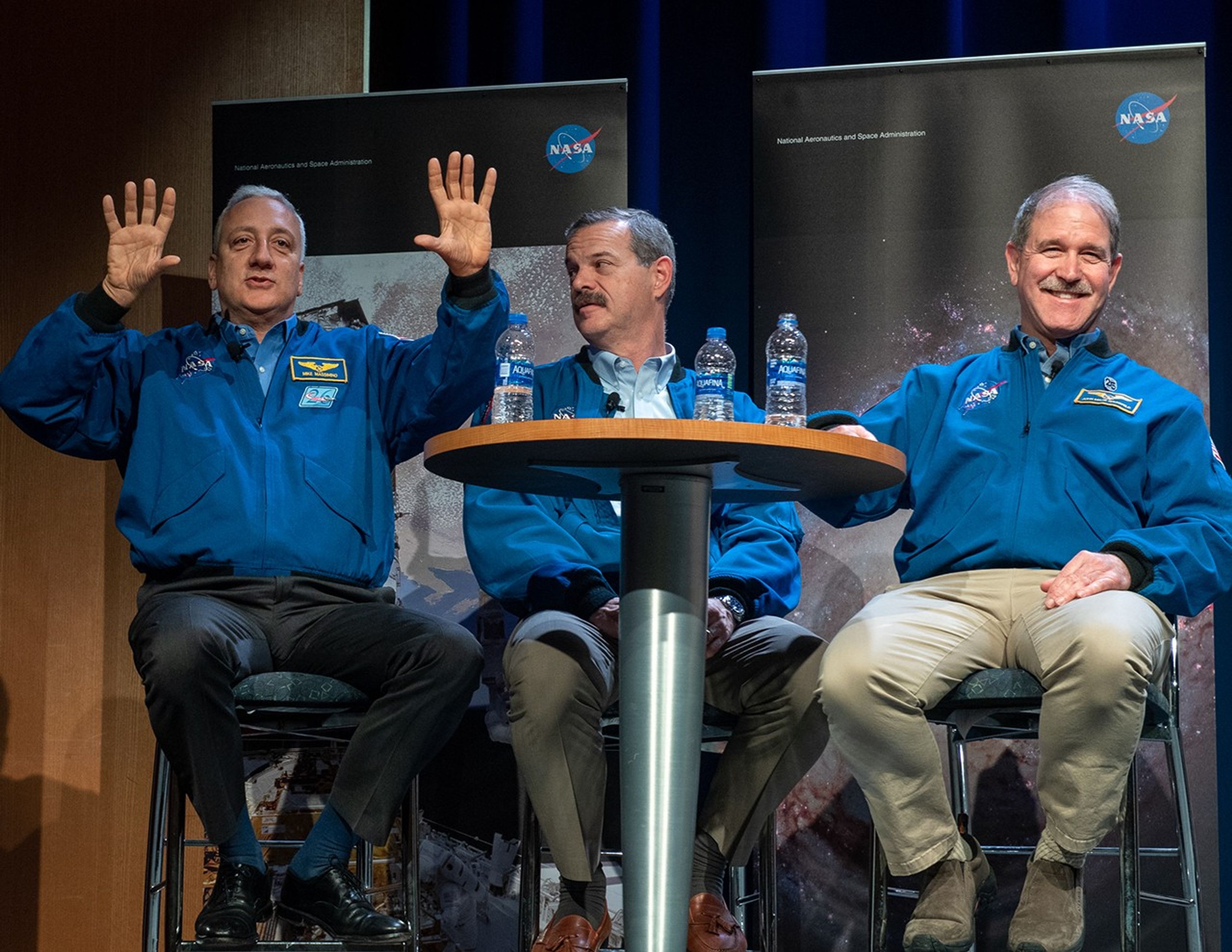 Mike Massimino (left) speaks to the audience while using his hands to visualize, while Scott Altman (center) looks at him and John Grunsfeld (right) smiles at the audience