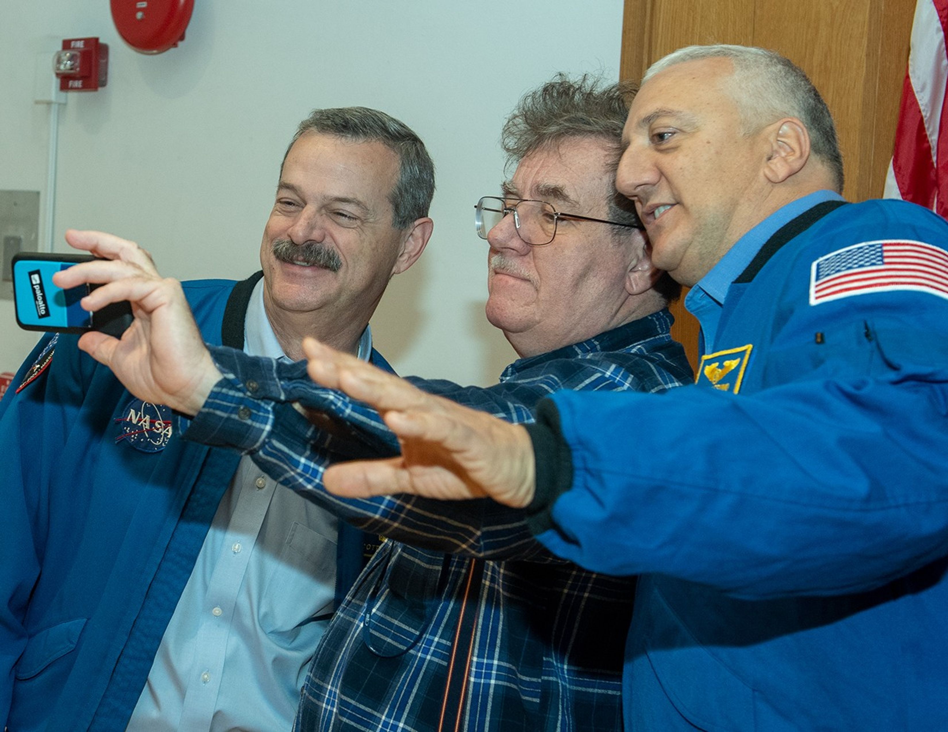 A male NASA employee (center) takes a selfie with two astronauts (left and right).
