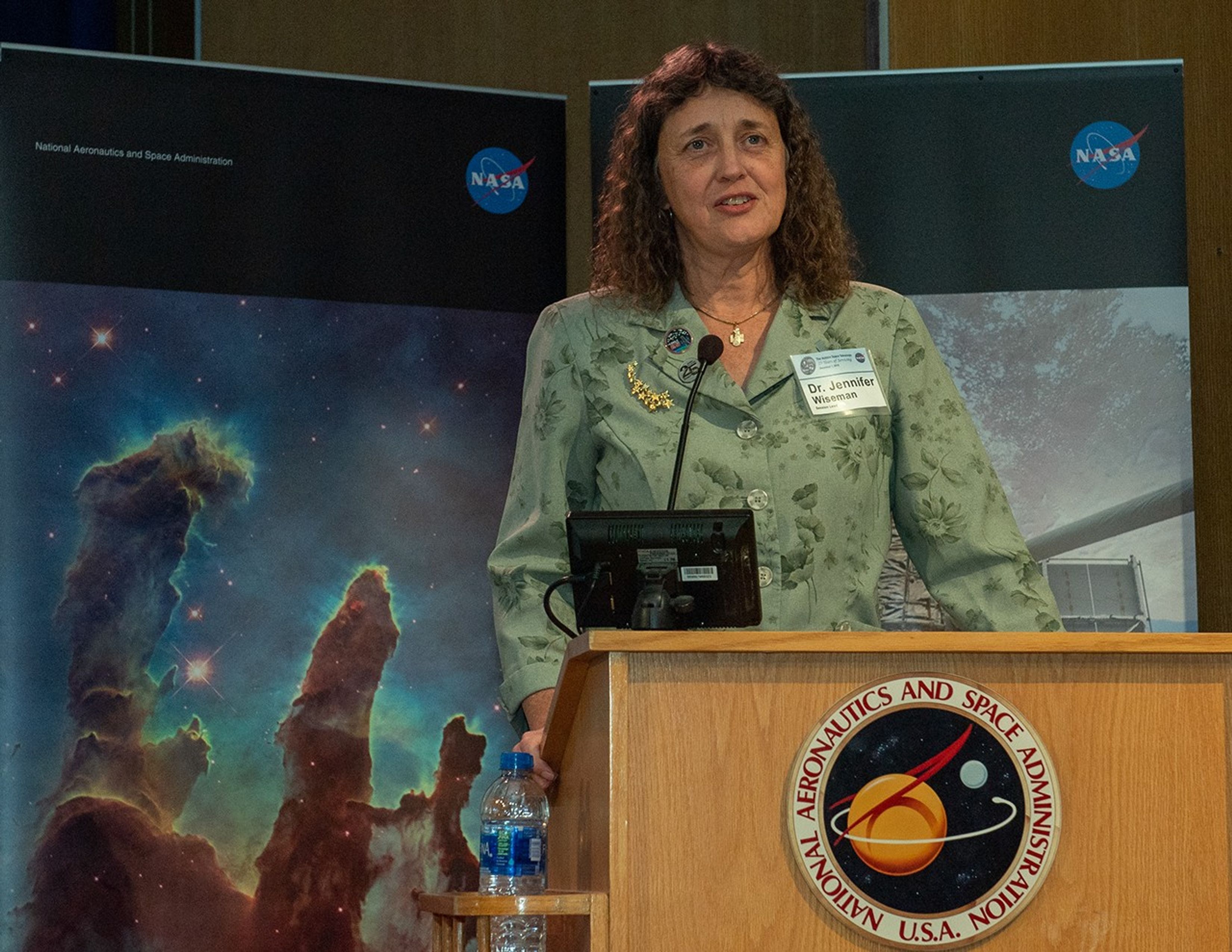 Dr. Jennifer Wiseman stands at the NASA podium, addressing the audience.