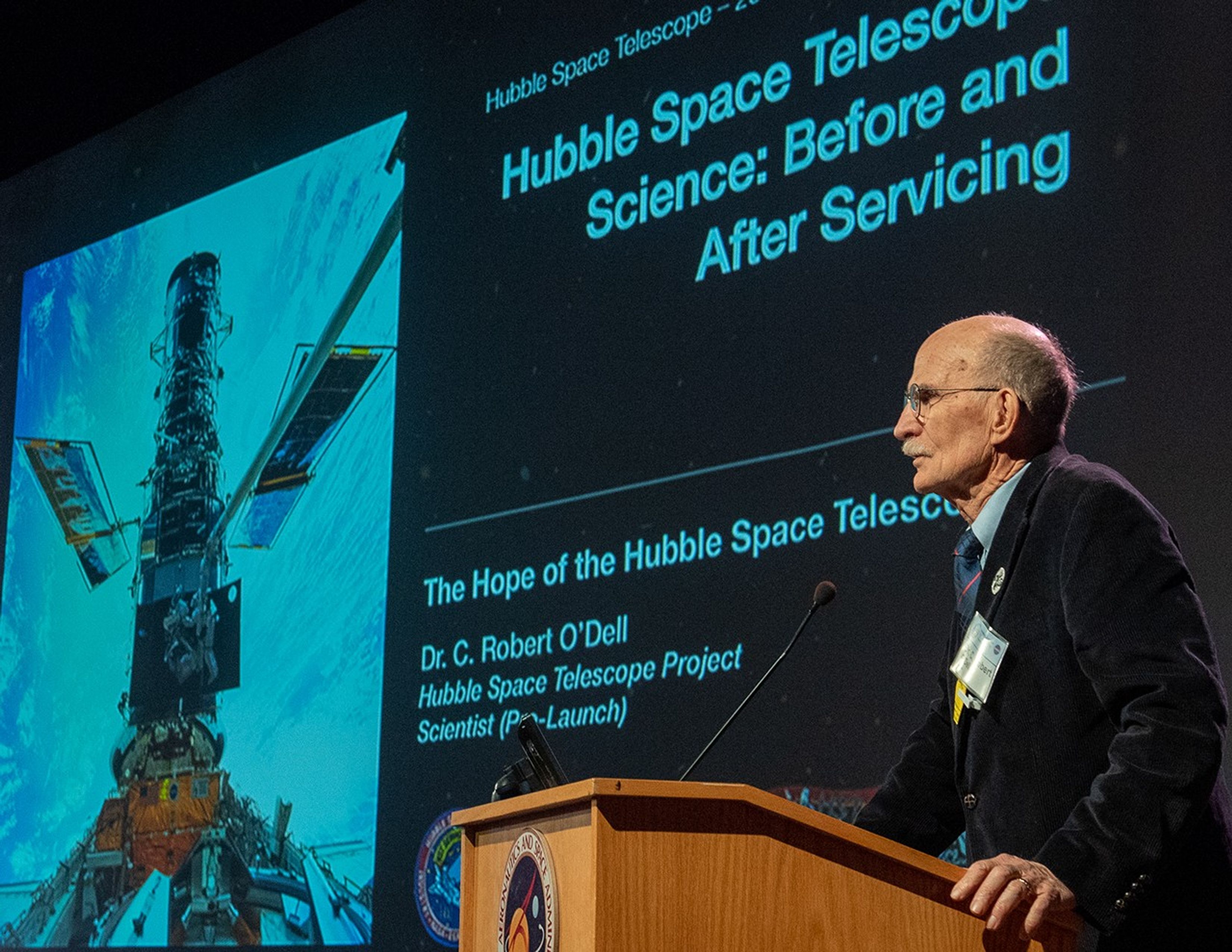 Dr. O'Dell speaks from the podium, with an introduction slide in the background.