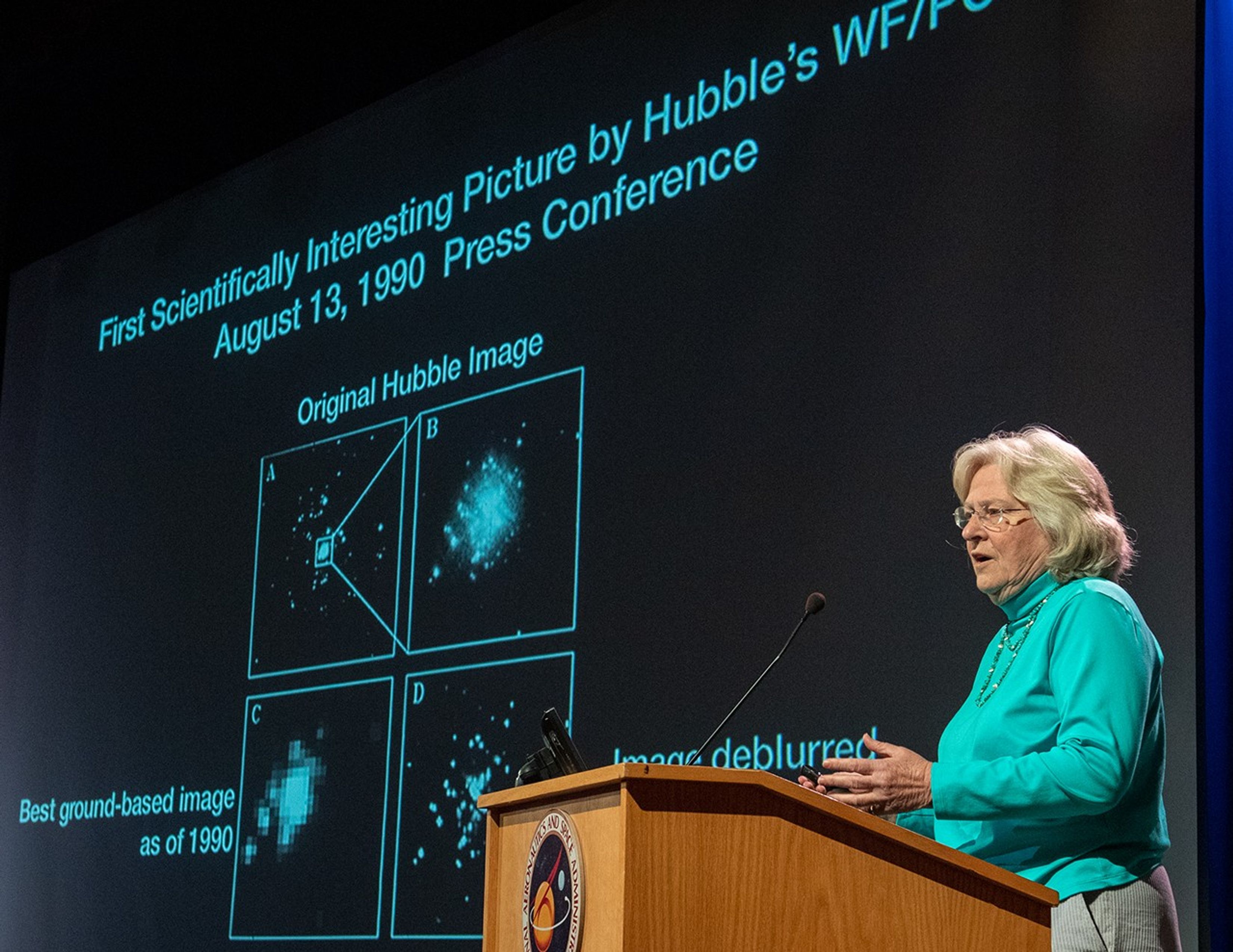 Sara Heap speaks from the podium, with a Hubble science image on the screen in the background.