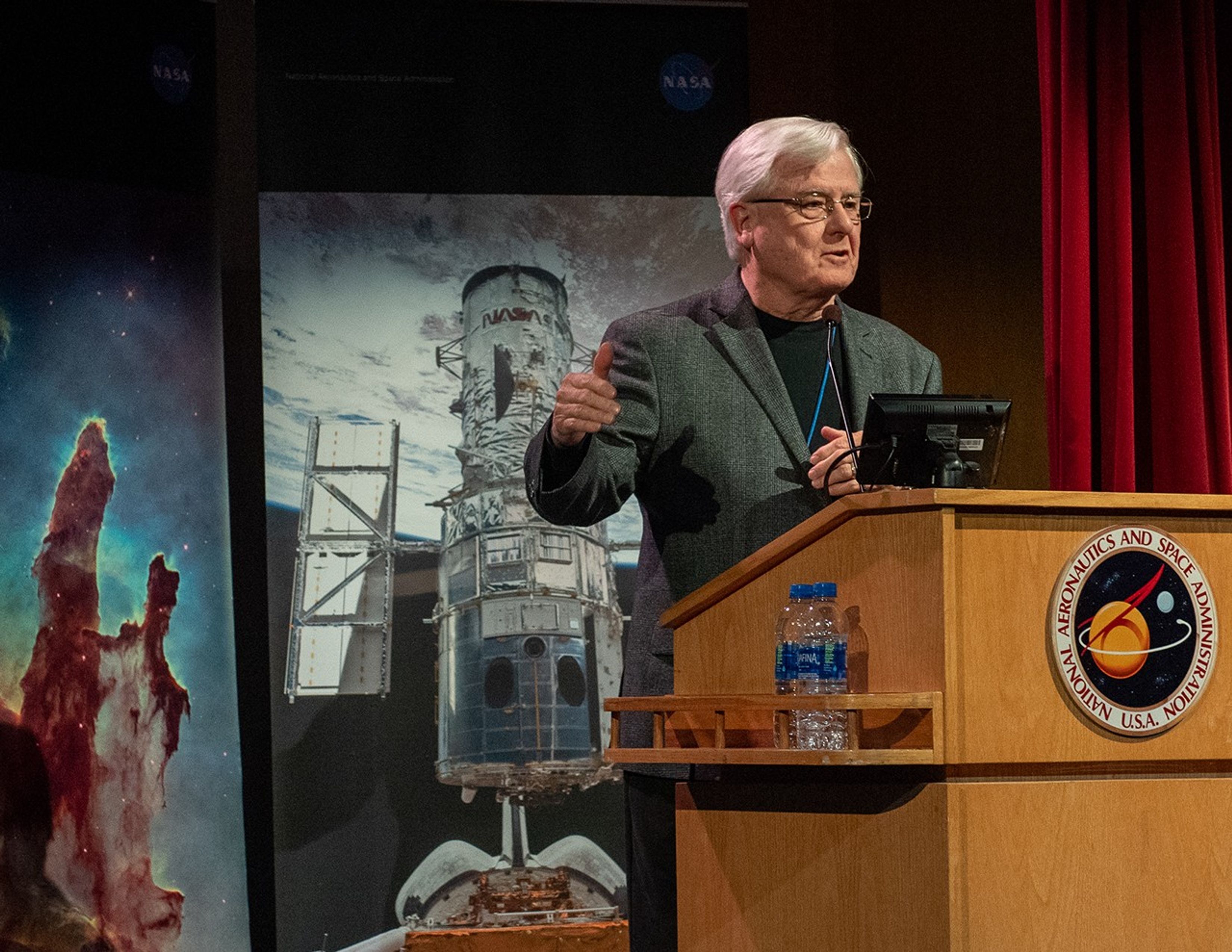 David Leckrone speaks from the NASA podium, with Hubble banners in the background.