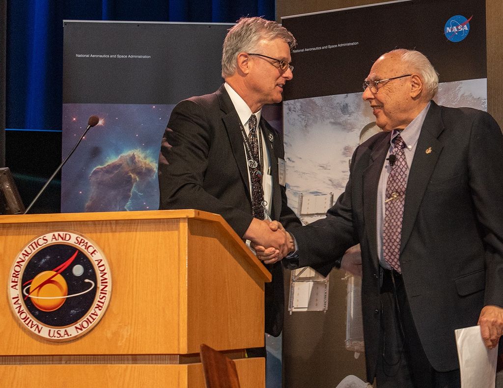 Jim Jeletic (left) and Frank Cepollina (right) shake hands at the NASA podium.