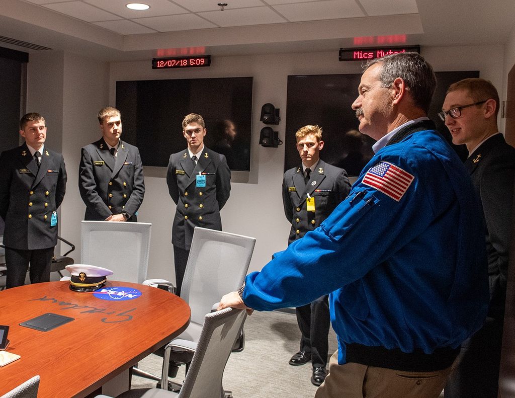 Scott Altman, second from the right, speaks to a group of Navy midshipmen, left (five men are visible in the image), around a conference room table.