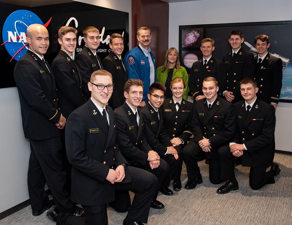 Scott Altman and Kay Hire (back center) take a photo with 13 visiting midshipmen (back left, back right, front), 12 men and 1 woman.