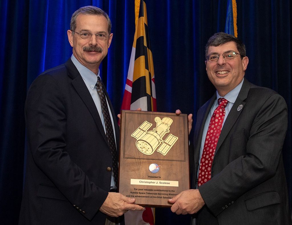 Altman (left) and Scolese (right) hold a wooden plaque between them with Scolese's name and a gold graphic of Hubble on it.