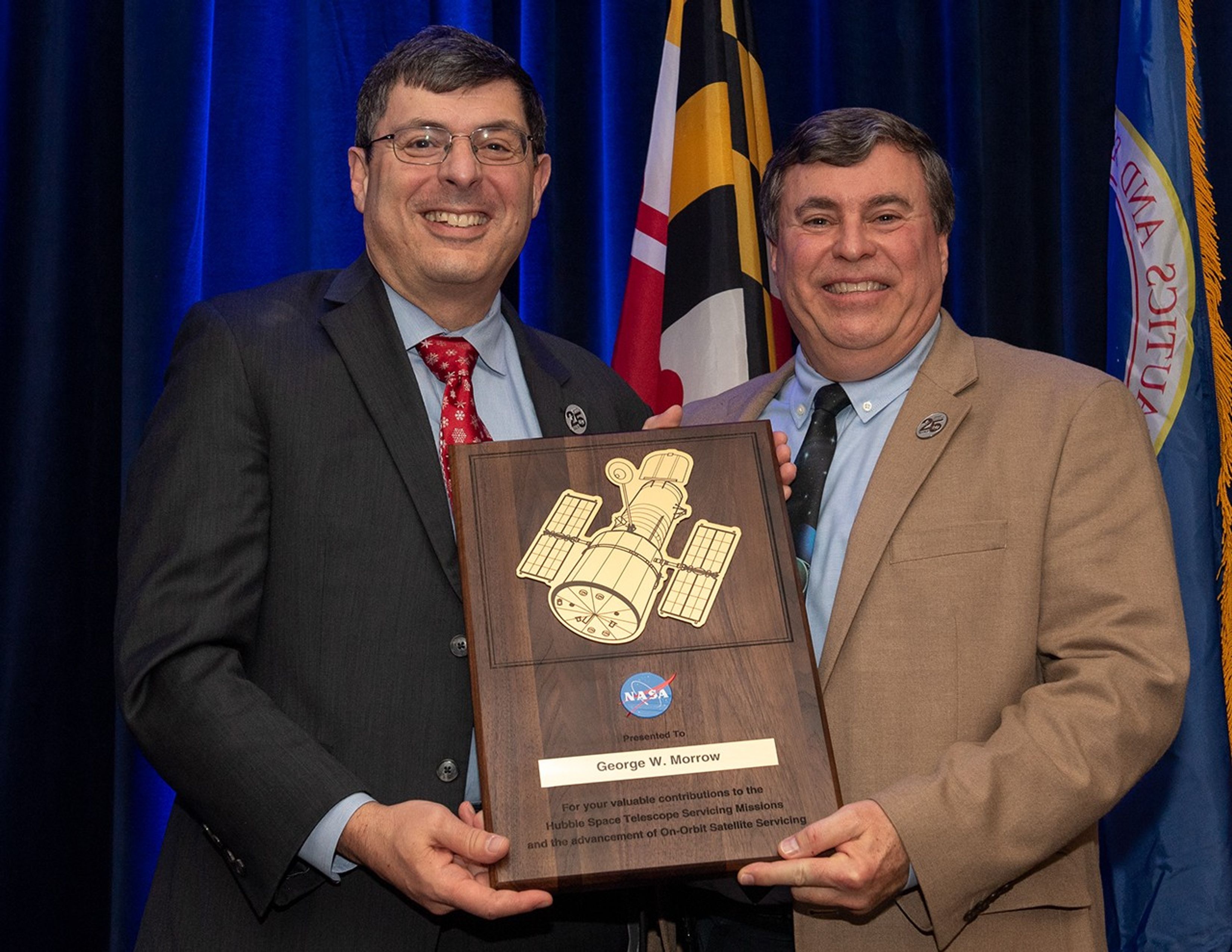 Scolese (left) and Morrow (right) hold a wooden plaque between them with Morrow's name and a gold graphic of Hubble on it.