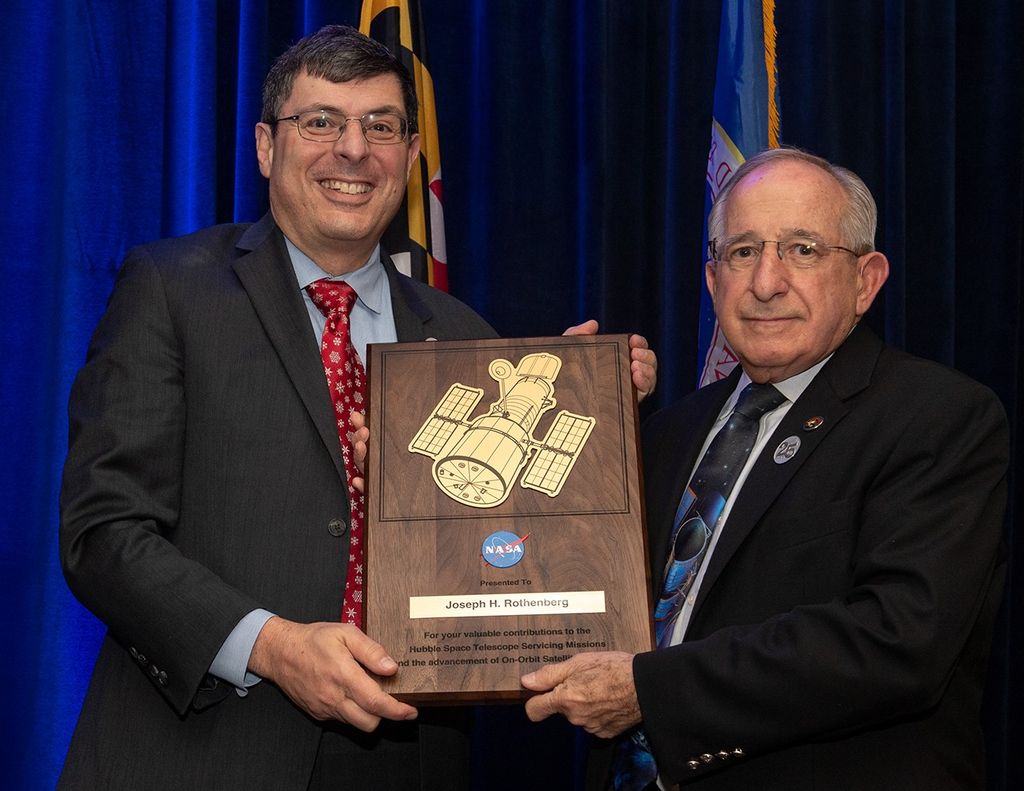 Scolese (left) and Rothenberg (right) hold a wooden plaque between them with Rothenberg's name and a gold graphic of Hubble on it.