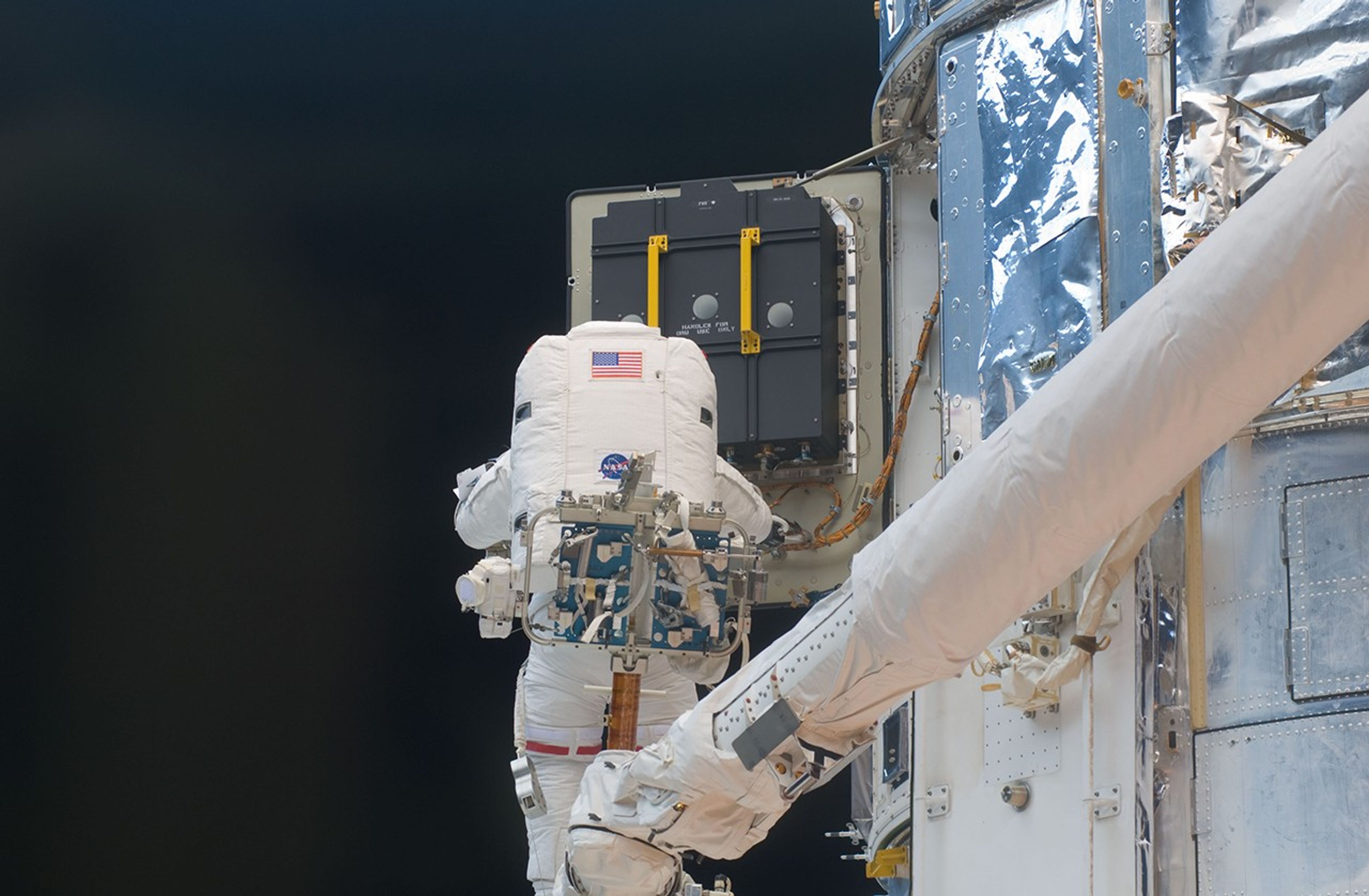 STS-125 Mission Specialist 3 (MS3) John Grunsfeld works to replace the Hubble Space Telescope's Support Systems Module (SSM) Equipment Section (ES) Bay 3 battery during the fifth session of Extravehicular Activity (EVA5). He is positioned on the Shuttle Remote Manipulator System (SRMS) Manipulator Foot Restraint (MFR).