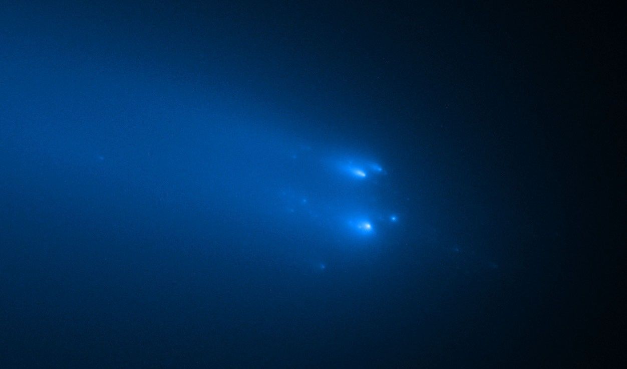 The comet breaks apart into several bright, fuzzy, blue, streaking lights in a line from left to right on a black background.