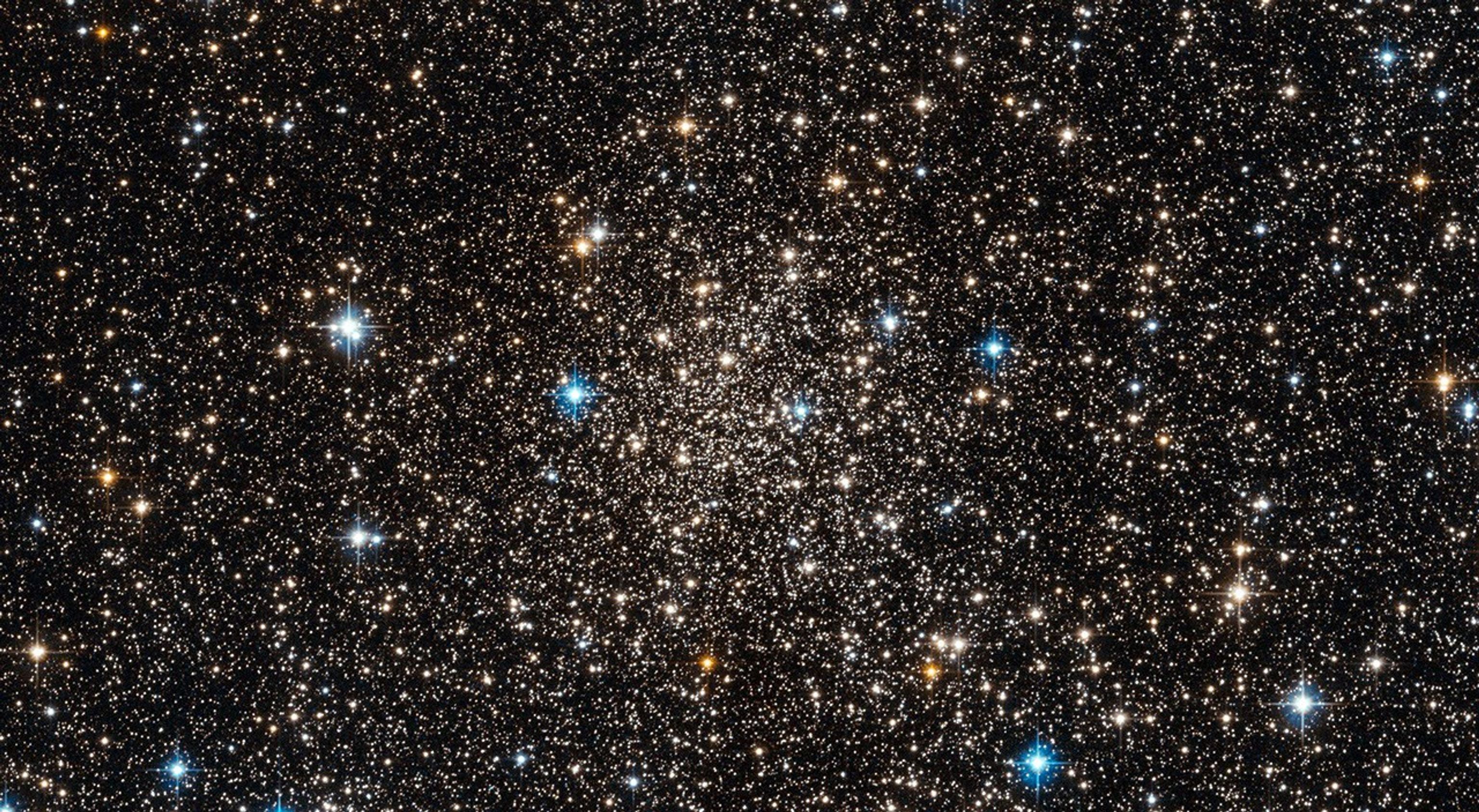 A cluster of white, blue-white, and orange stars, more densely concentrated at the center.