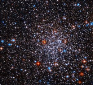 Bright stars cluster against a black background. The stars are more densely concentrated in the center of the image. The stars appear mostly white, but bright red and blue stars are also visible sprinkled throughout the image.