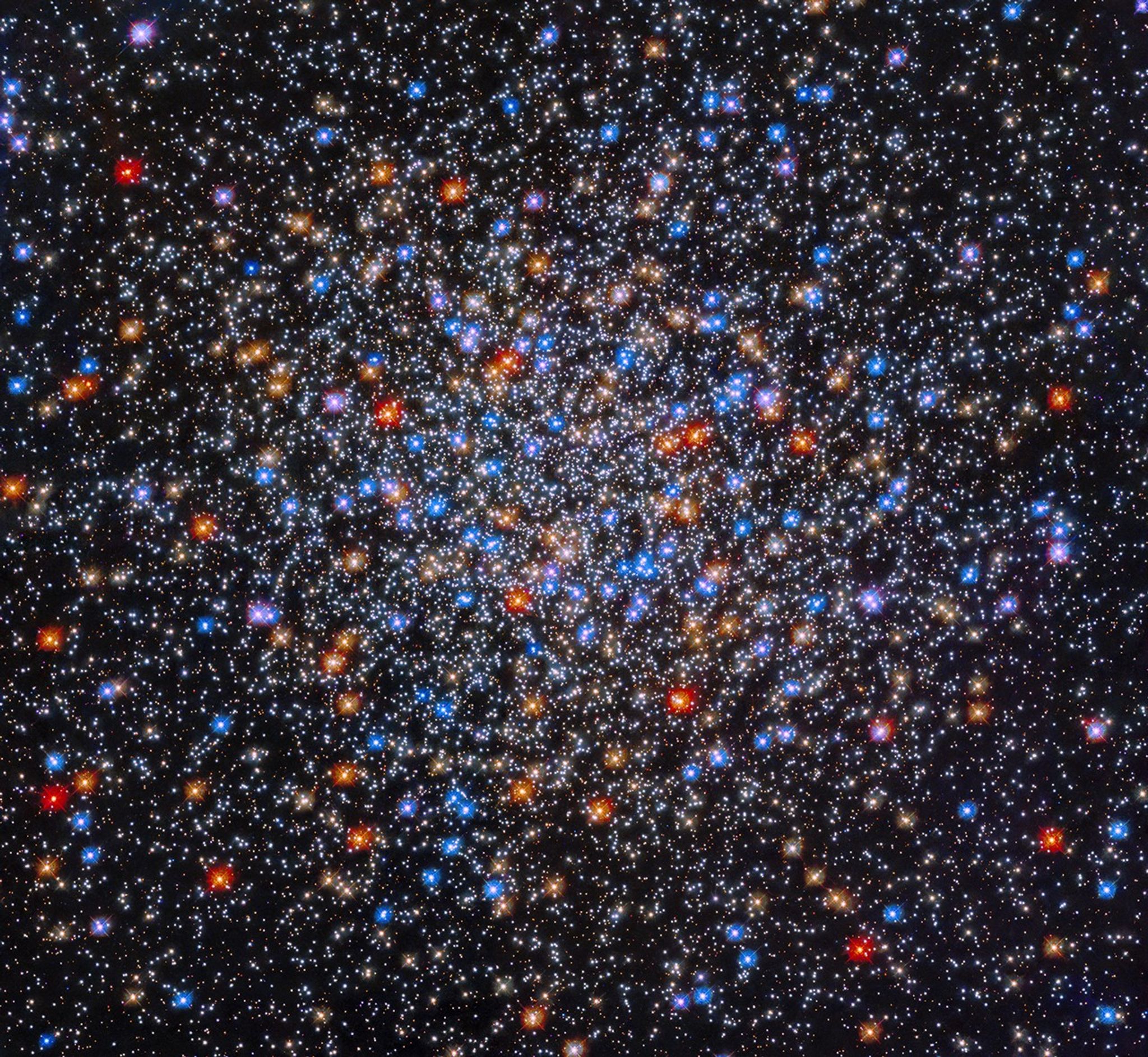 A colorful grouping of red, yellow, orange, blue, and white stars sits at image center. The stars appear close together at image center and appear less dense as you move outward.