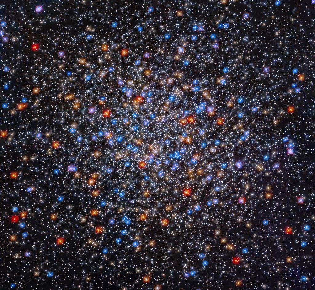 A colorful grouping of red, yellow, orange, blue, and white stars sits at image center. The stars appear close together at image center and appear less dense as you move outward.
