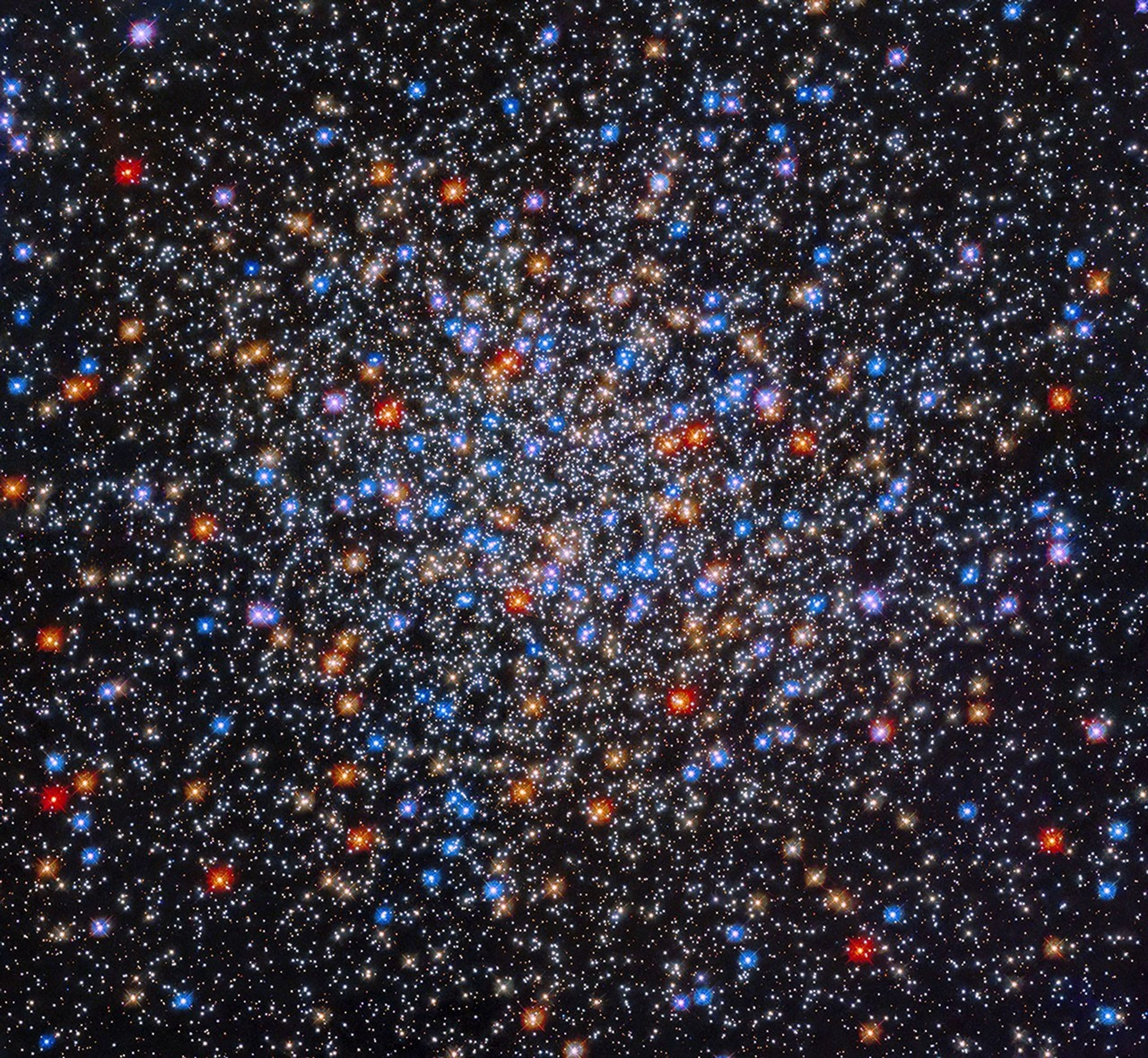 A colorful grouping of red, yellow, orange, blue, and white stars sits at image center. The stars appear close together at image center and appear less dense as you move outward.