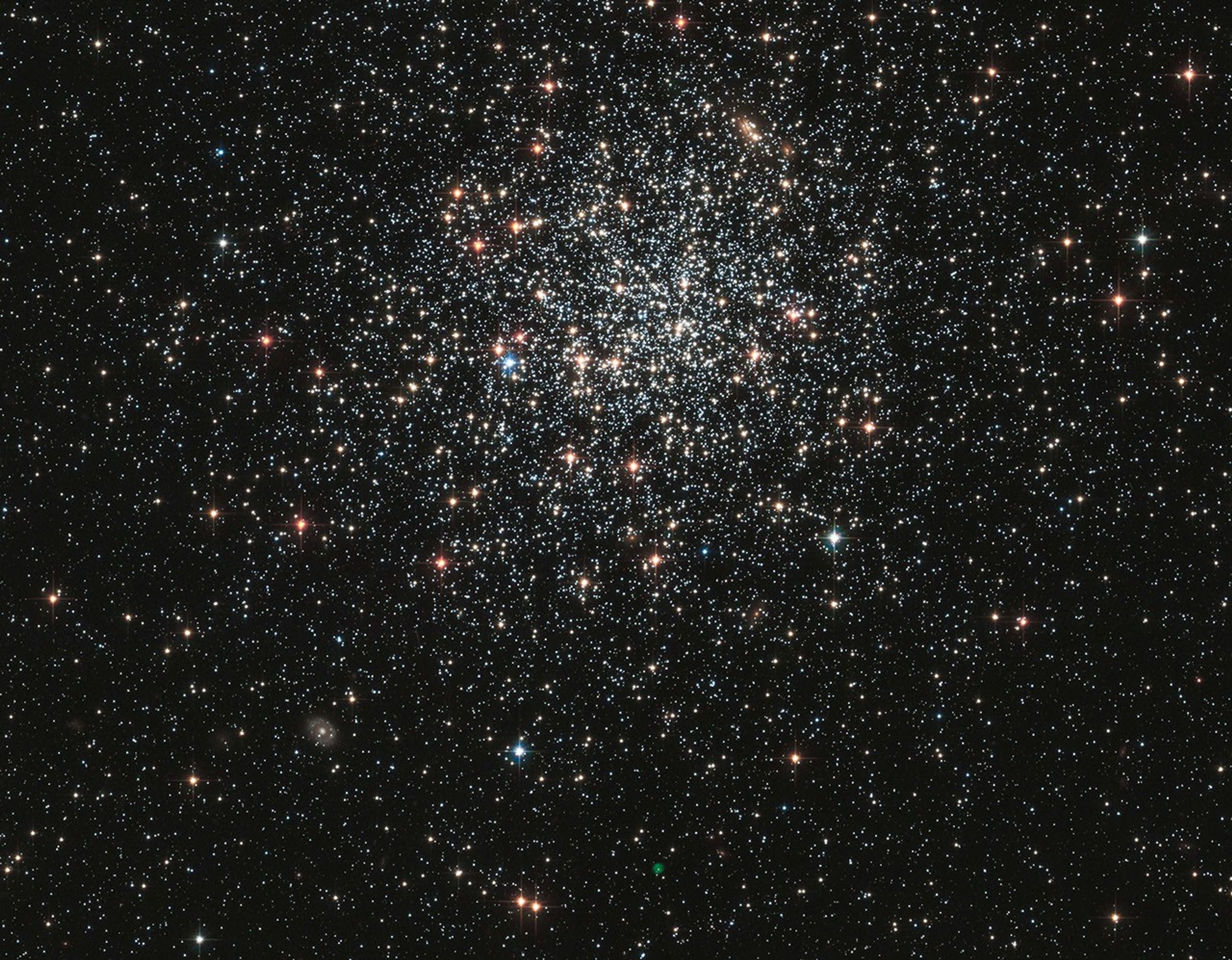 White, red-orange, and a few blue stars packed tightly near the center in a sphere-shape, and thinning out farther from the center.