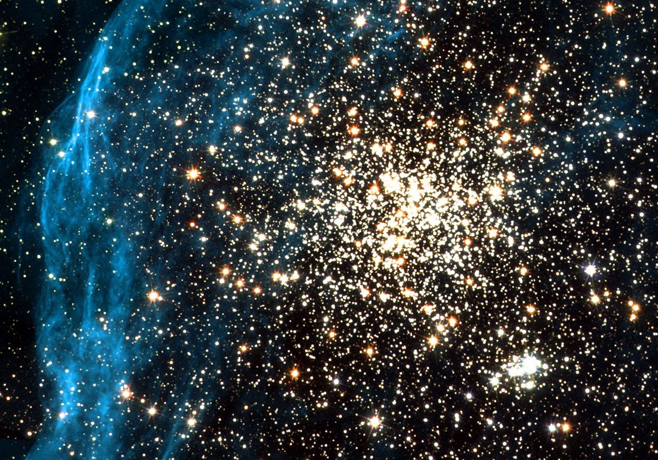 A nearly spherical gathering of yellow, orange, and white stars at center top. Blue gas cloud extends from top left to center bottom.