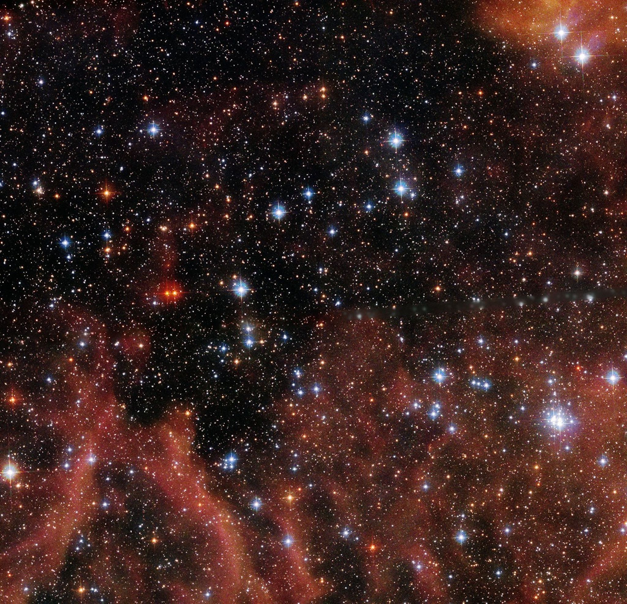 A couple of dozen bright stars in the foreground, mostly blue-white but some red-orange. Red-orange gas and dust in the background along the bottom half of the image and in the top-right corner. Thousands more stars in the background, scattered throughout.