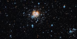 A thick glob of blue-white stars and red-orange stars near the center. Smaller groupings of blue-white stars farther out.