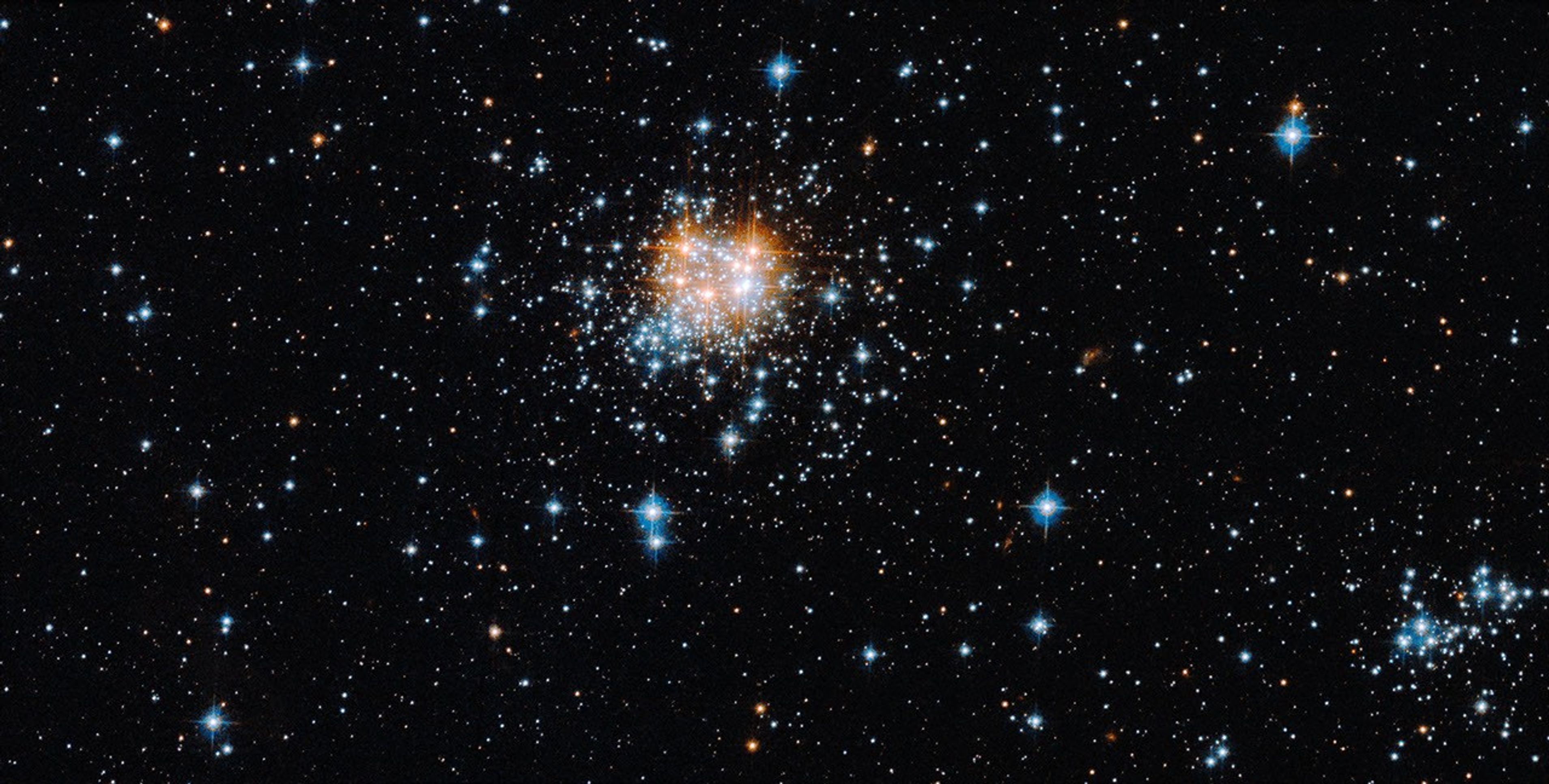 A thick glob of blue-white stars and red-orange stars near the center. Smaller groupings of blue-white stars farther out.