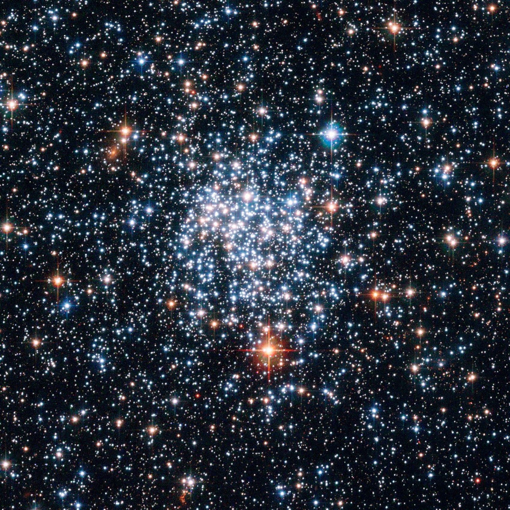 Blue and red stars shine in the foreground, with thousands more stars of all colors (mainly red, orange, white, and blue) in the background.
