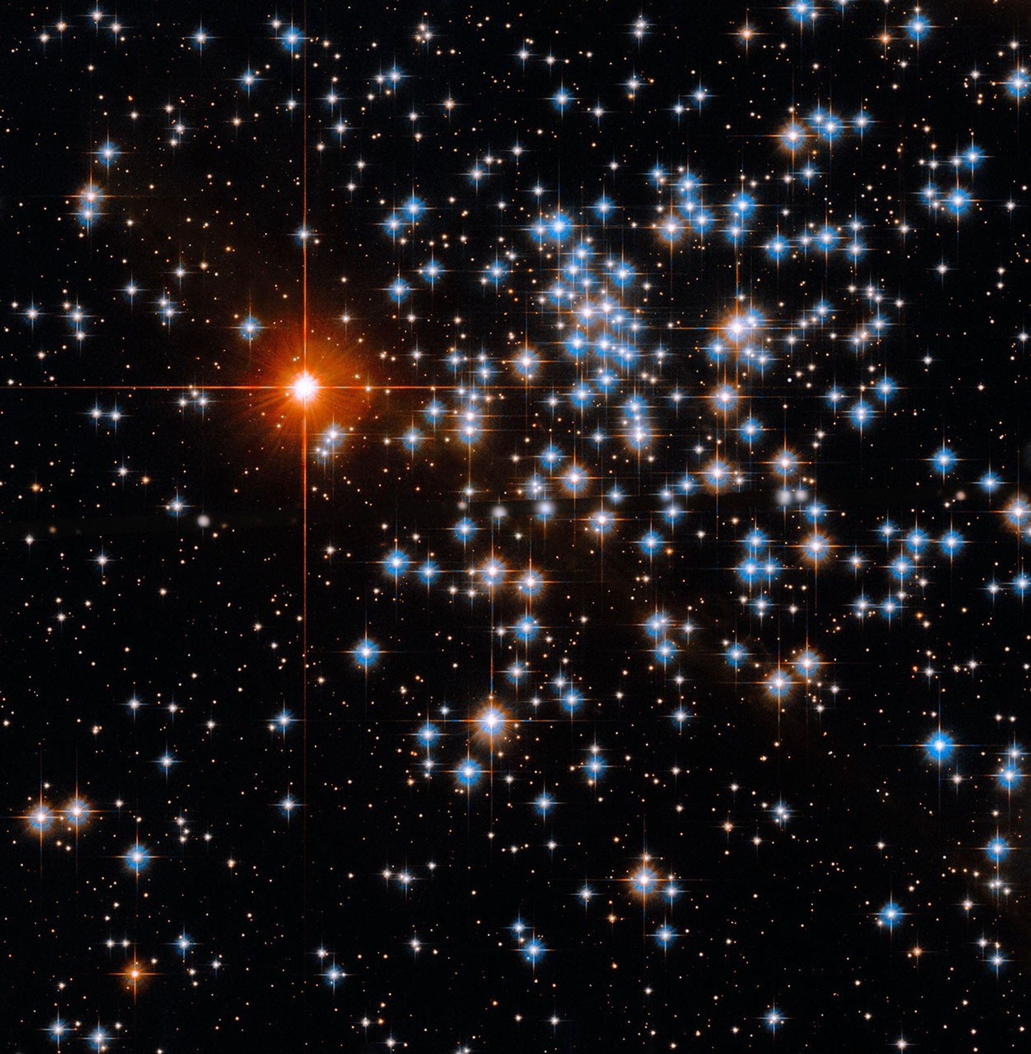 A smattering of bluish-white and reddish-white stars, more plentiful on the right side of the image. On the left side shines a much brighter red-orange star.