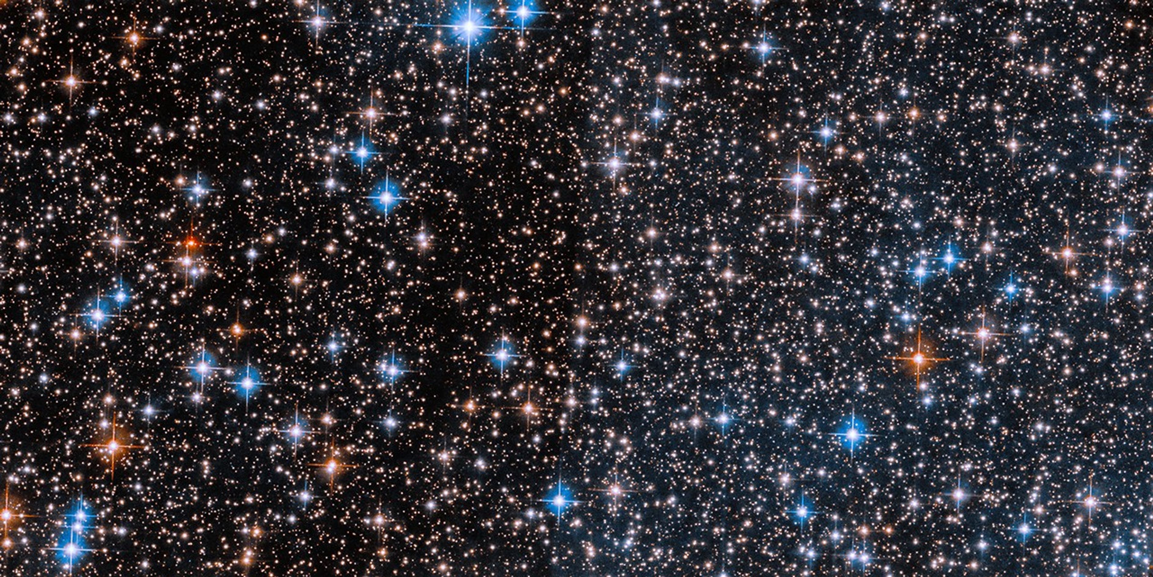 A field of stars of various colors, including red, white and blue. Some dark patches are scattered among the thickly collected stars.