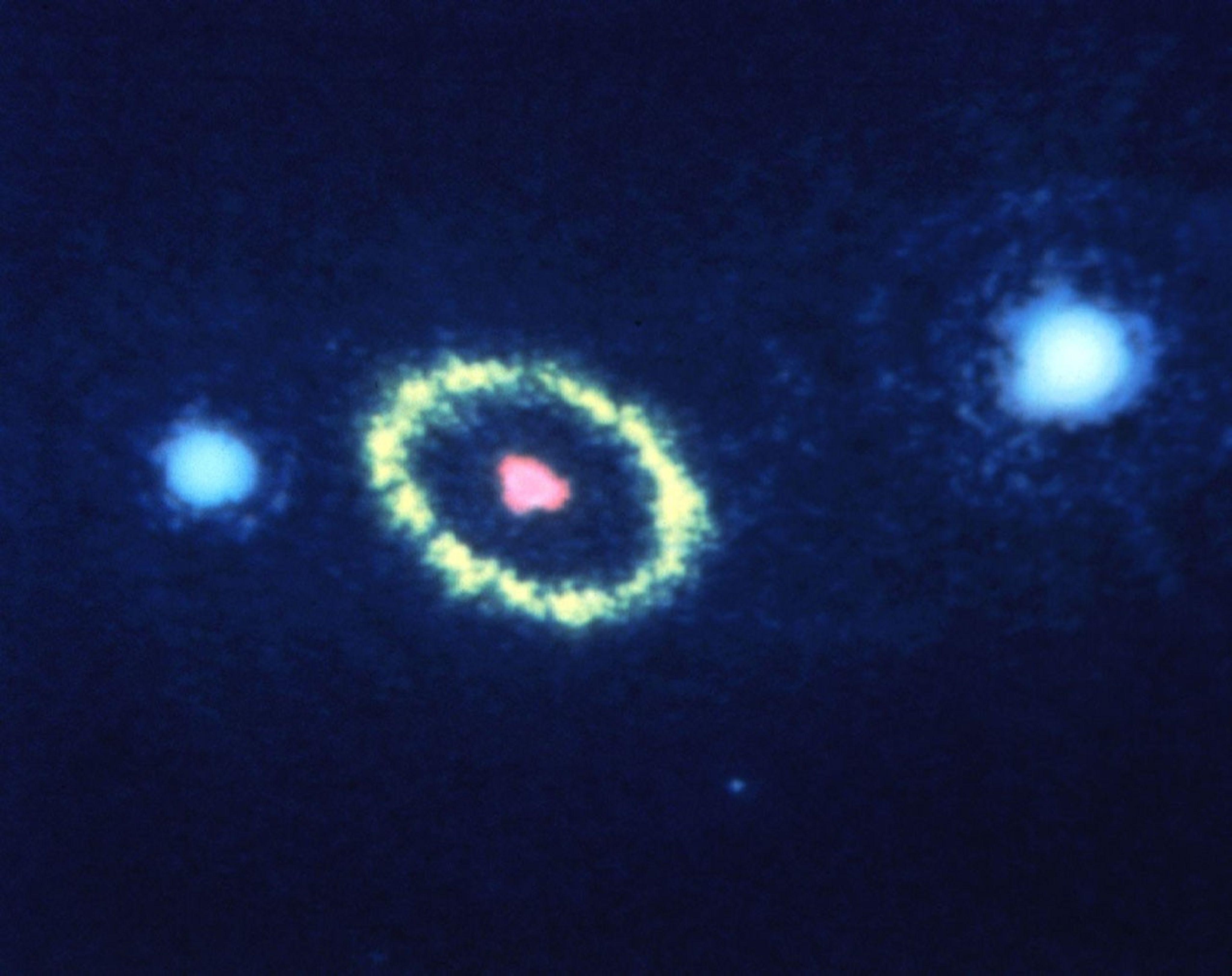 Dark blue background. near image center is a pink  blob surrounded by a yellow ring. On either side of the ring are blue-white blobs.