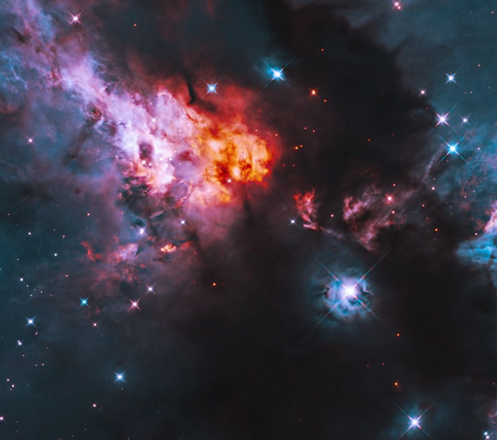 Shining blue stars are sprinkled throughout glowing clouds of orange, pink and bluish gas, alongside dark clouds of dust. A particularly bright star shines against the inky dark dust of the lower right quadrant.