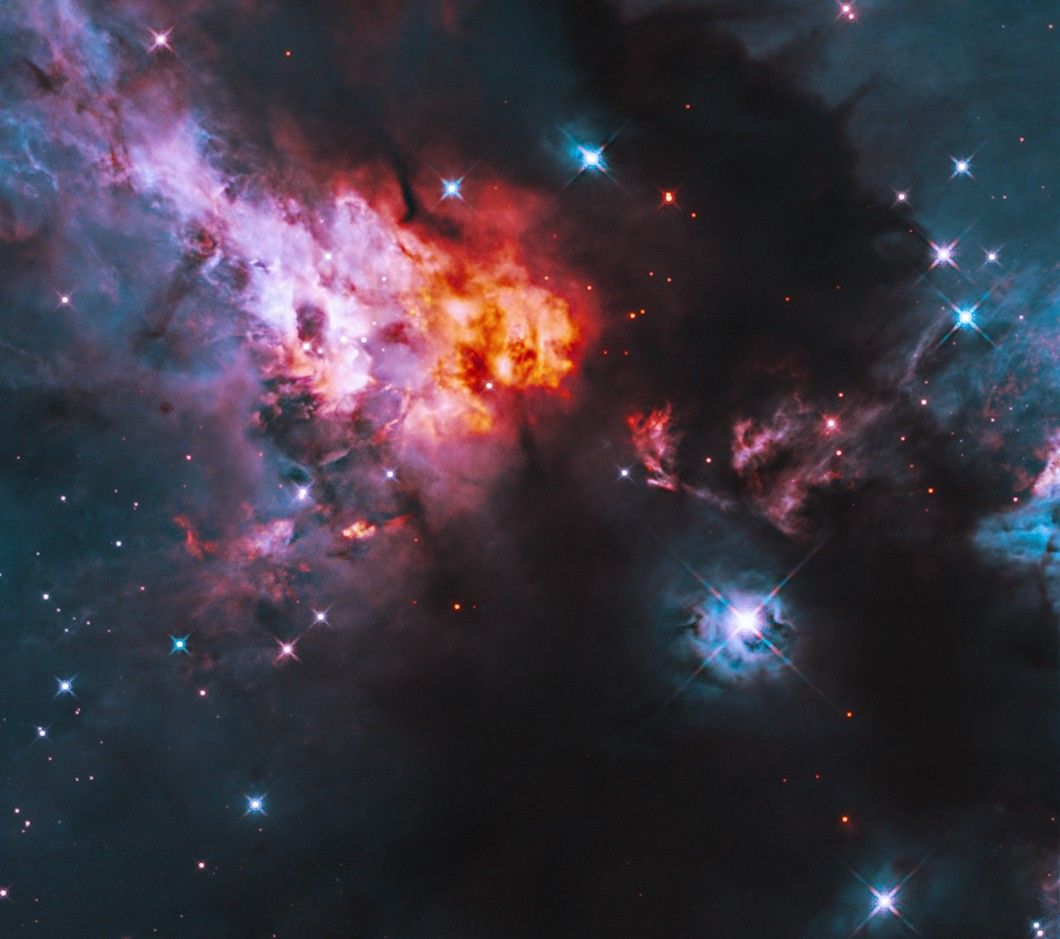 Shining blue stars are sprinkled throughout glowing clouds of orange, pink and bluish gas, alongside dark clouds of dust. A particularly bright star shines against the inky dark dust of the lower right quadrant.