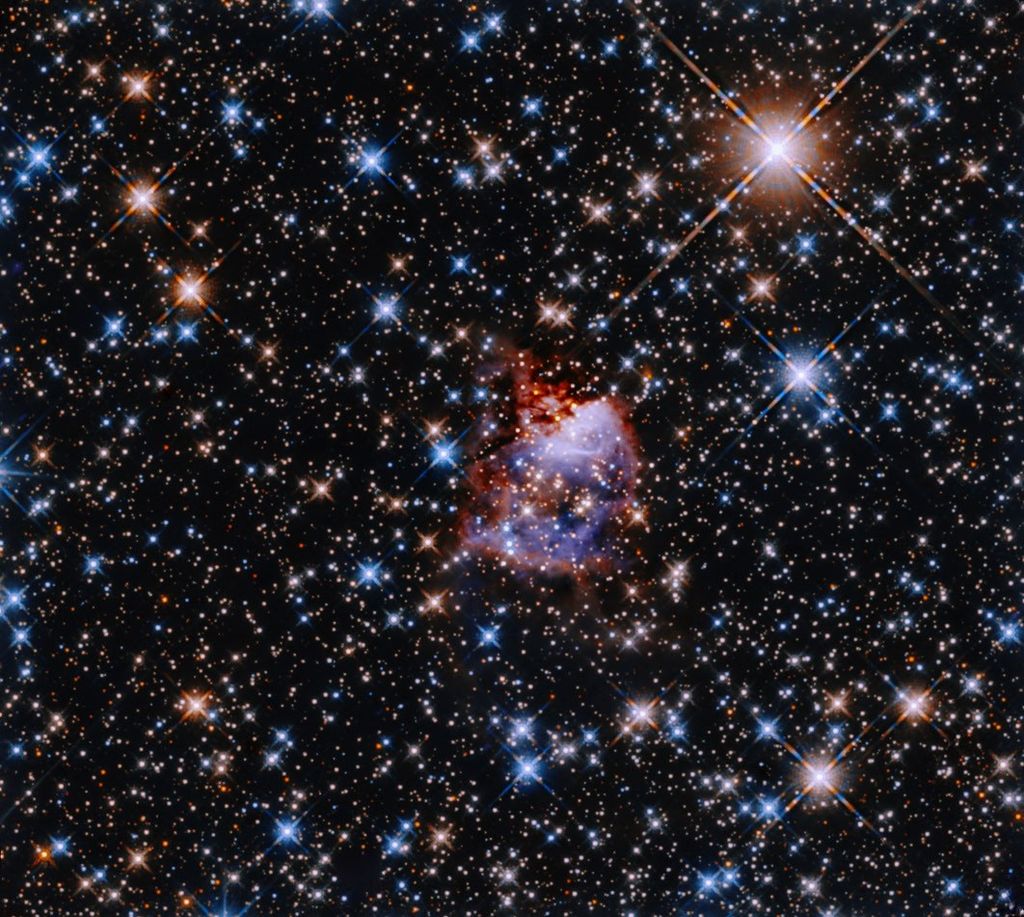 A small, bluish cloud edged in red gas is in the center of a field thick with multicolored stars.