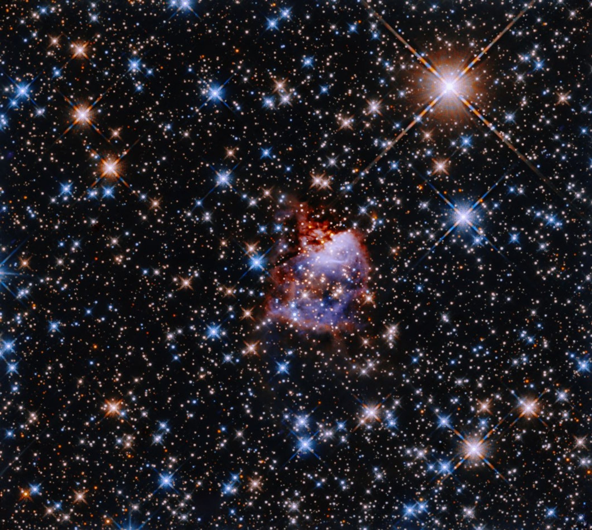 A small, bluish cloud edged in red gas is in the center of a field thick with multicolored stars.