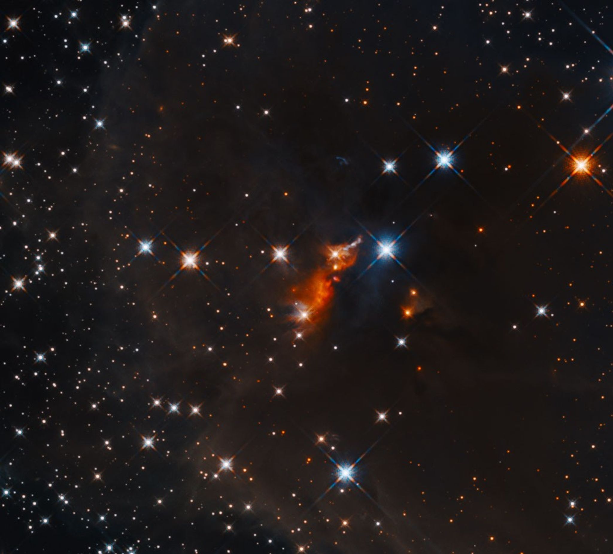 A bright, glowing cloud of orange gas is situated in the center of dark dust clouds and a field of stars.