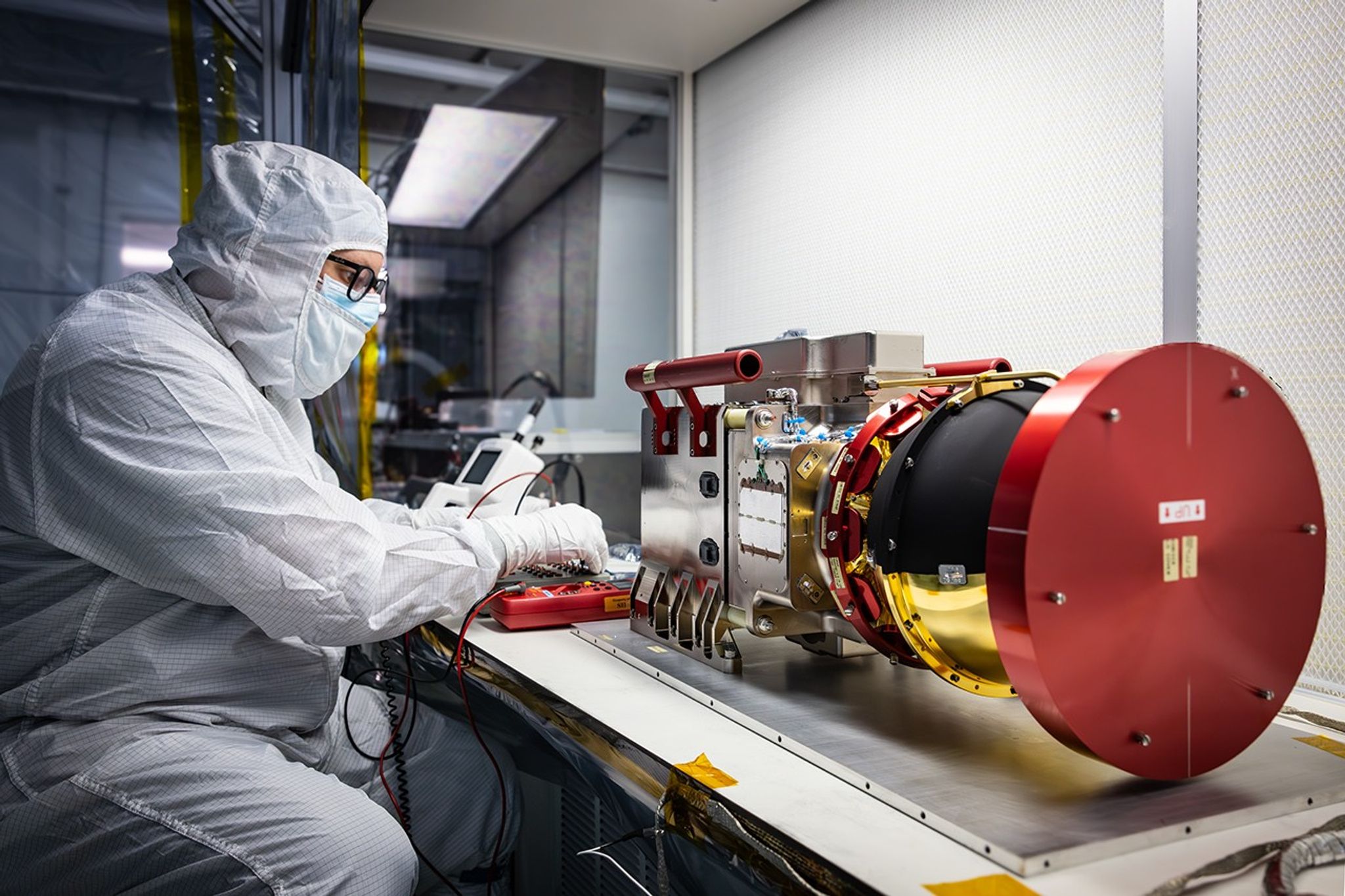 Image shows technician in a white bunny suit testing the Compact Dual Ion Composition Experiment (CoDICE) instrument of NASA’s IMAP (Interstellar Mapping and Acceleration Probe) observatory  at Astrotech Space Operations Facility near the agency’s Kennedy Space Center in Florida on Tuesday, June 17, 2025.