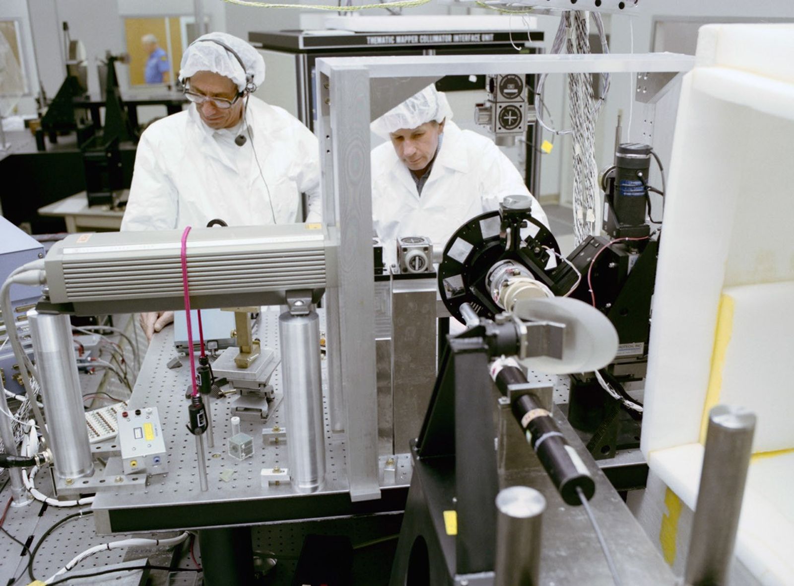 Two clean room technicians working with optical testing and calibration equipment for Landsat 4.