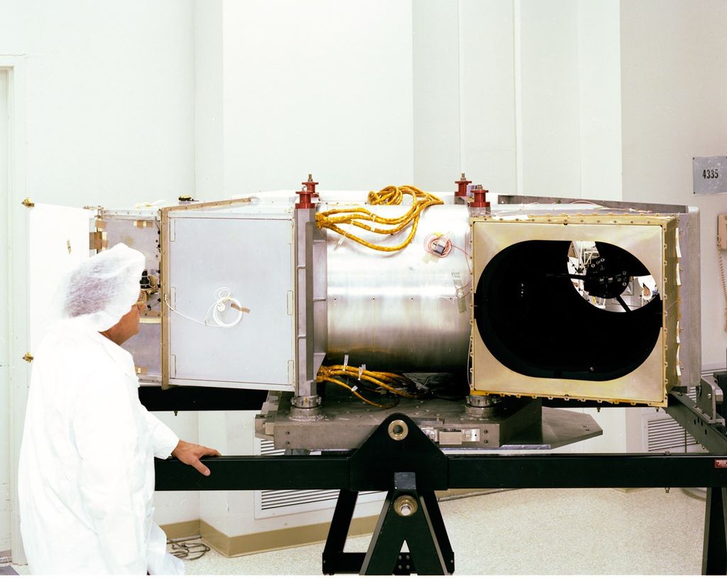 Technician in clean room attire inspecting the Thematic Mapper instrument during pre-launch preparation, showing the scanning aperture and internal components before installation on the Landsat 4 satellite.