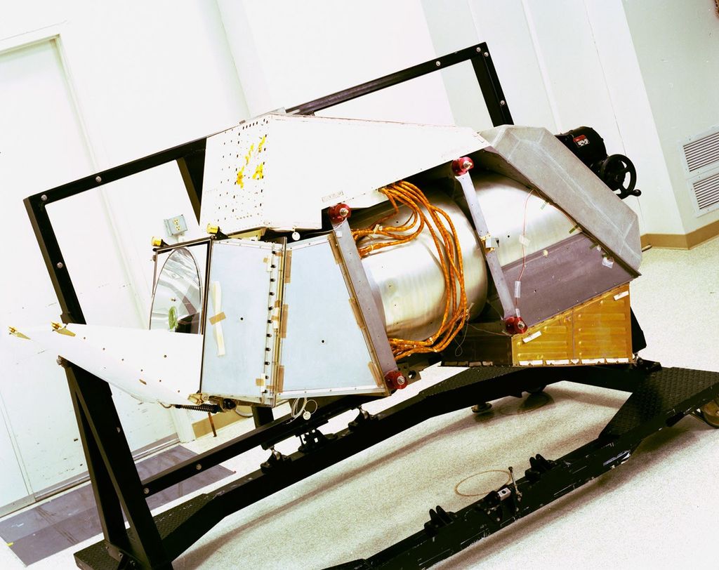 Landsat 4's Thematic Mapper instrument mounted on a test stand in a clean room, showing its metallic housing with exposed internal components and orange wiring harnesses.