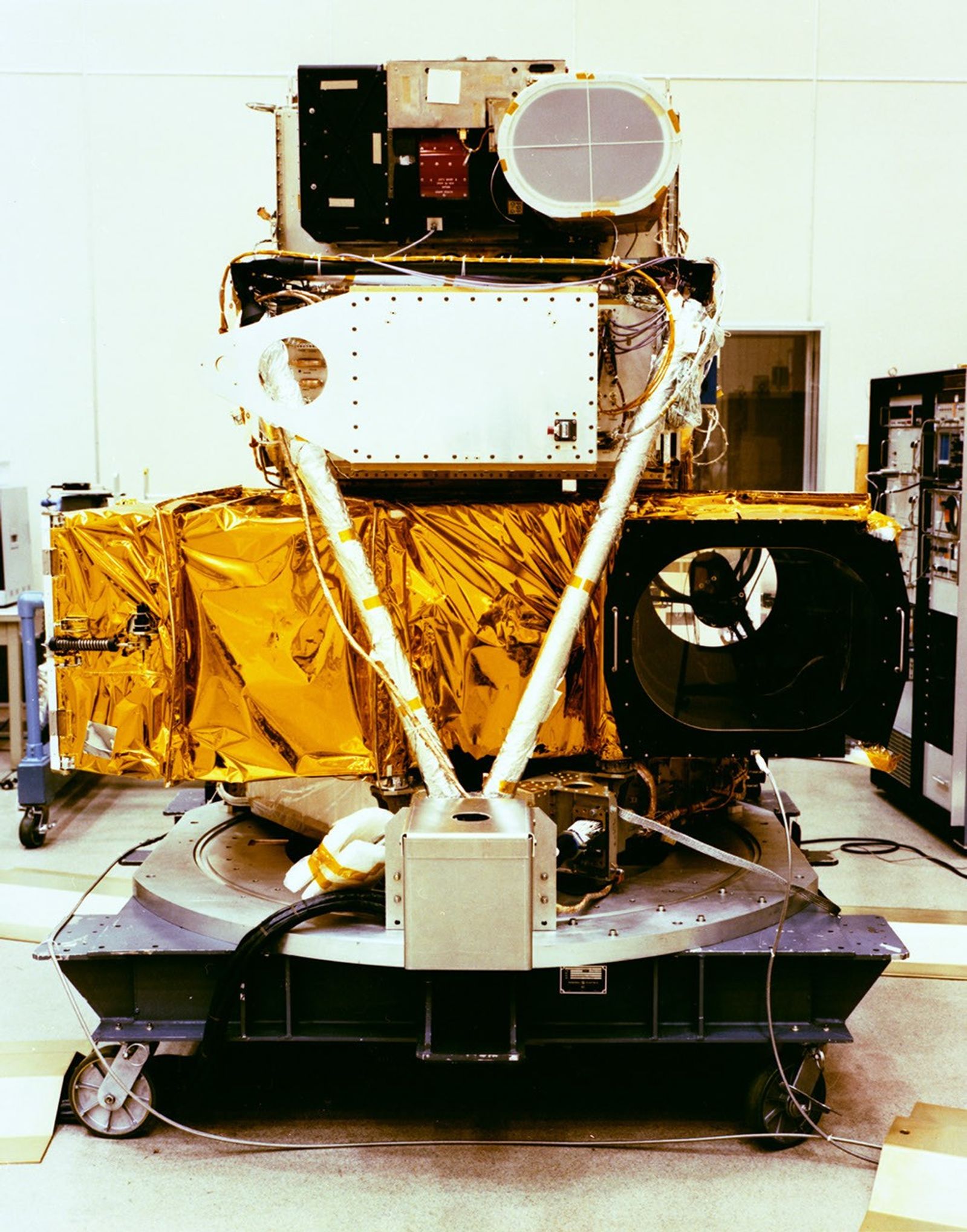Bottom view of Landsat 4 satellite during assembly, showing gold thermal blankets, white structural elements, and instrument components including circular aperture.