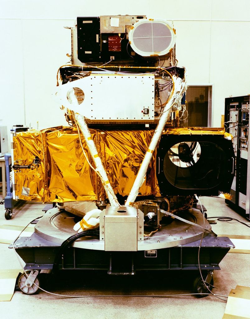 Bottom view of Landsat 4 satellite during assembly, showing gold thermal blankets, white structural elements, and instrument components including circular aperture.