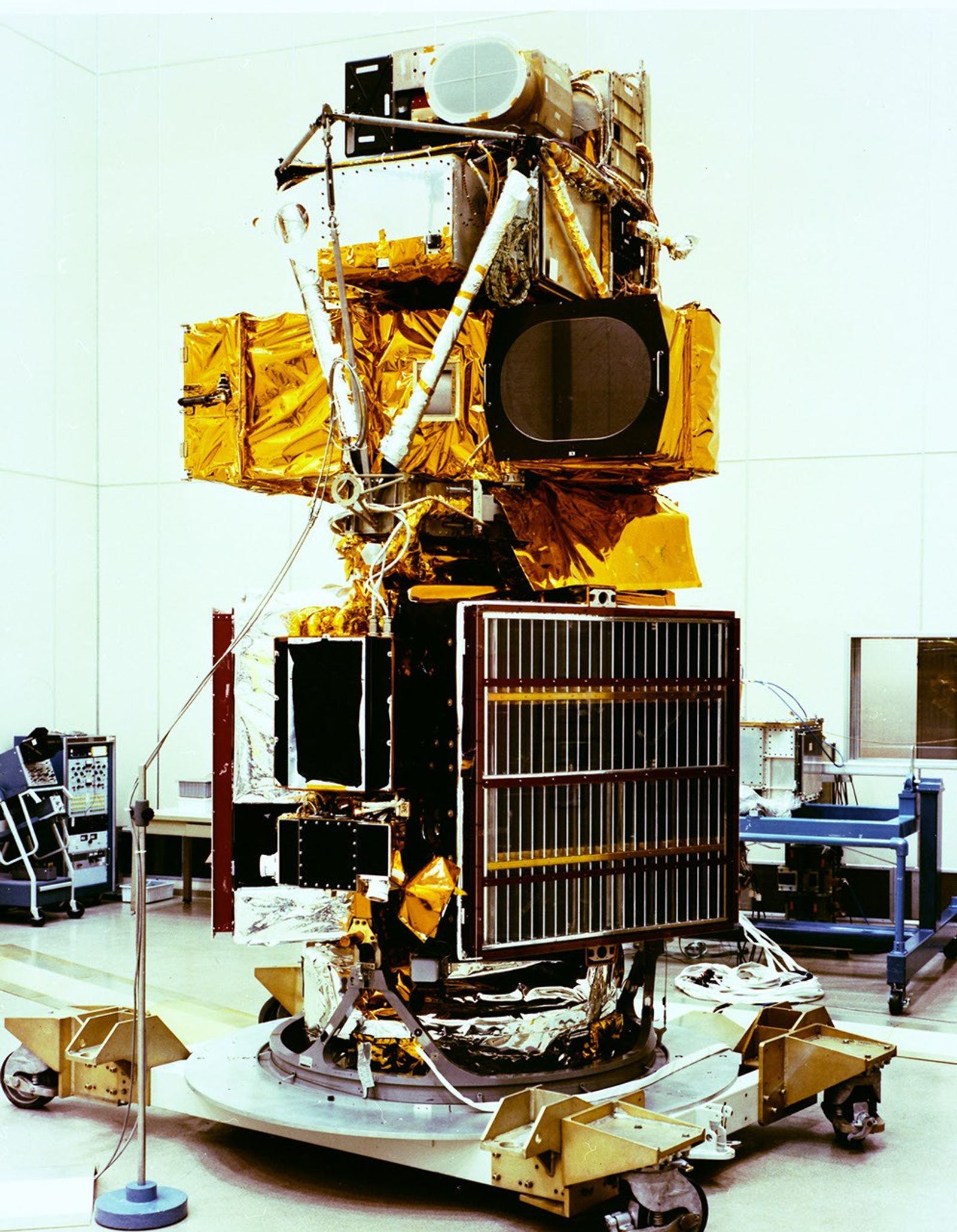 Landsat 4 satellite during assembly showing gold thermal blankets, solar panels, instruments, and white structural components on work platform.
