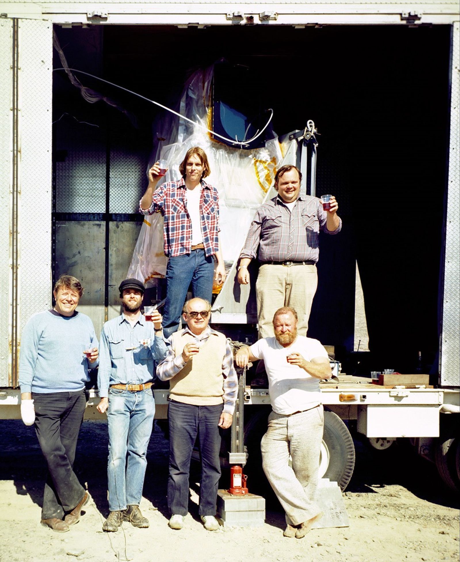 Field team celebrating during Landsat 5 TM mountain expedition with mobile ground station equipment visible in background.