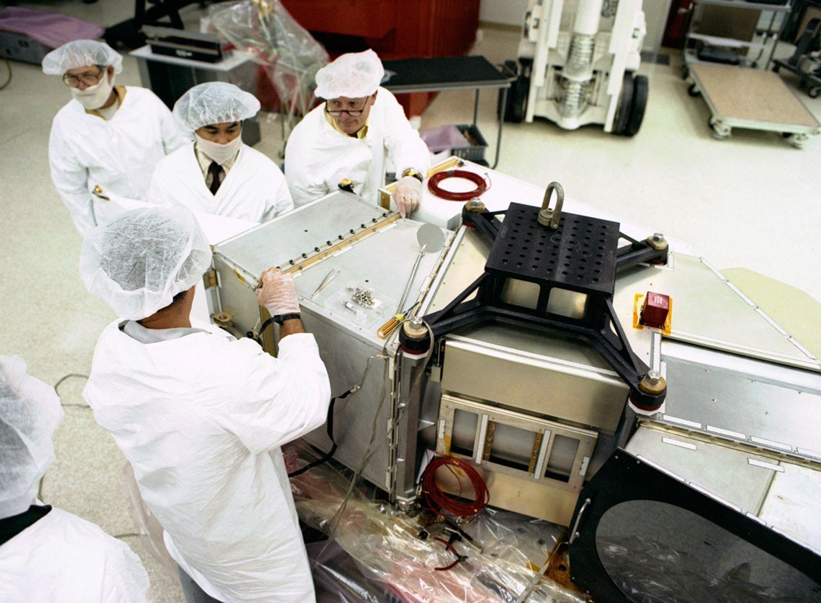 Team of four clean room technicians working on the assembly of the Landsat 5 Thematic Mapper instrument, installing components on its metallic housing structure.