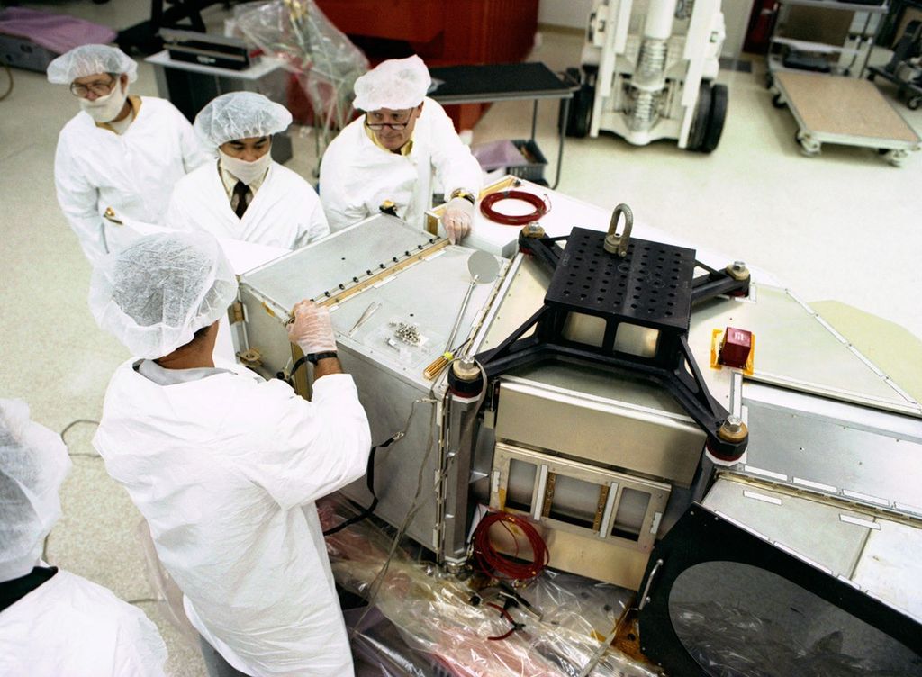 Team of four clean room technicians working on the assembly of the Landsat 5 Thematic Mapper instrument, installing components on its metallic housing structure.