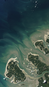A Landsat satellite image featuring tan and green shallow water contrasted with the dark blue ocean