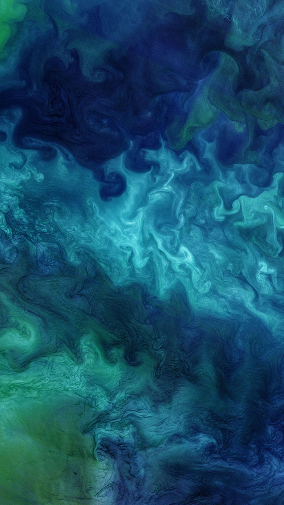 A Landsat satellite image of light and dark blue and green phytoplankton swirling across the ocean.