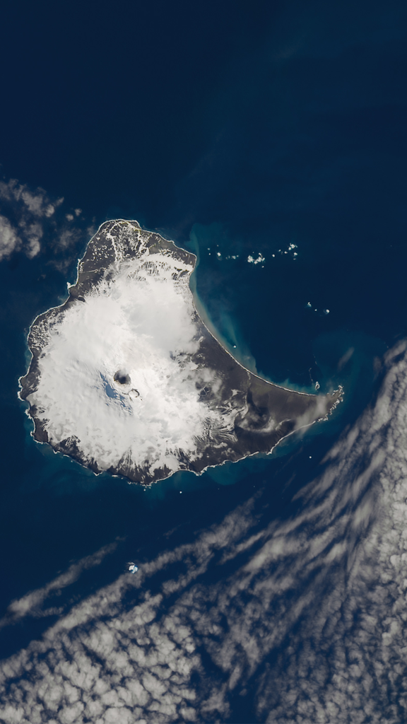 A Landsat satellite image of a small island covered in white snow surrounded by dark blue ocean.