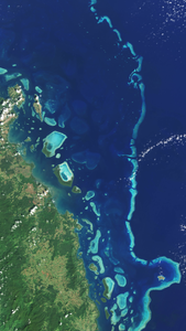 A Landsat satellite natural-color image of light blue coral peeking through the deep blue ocean.