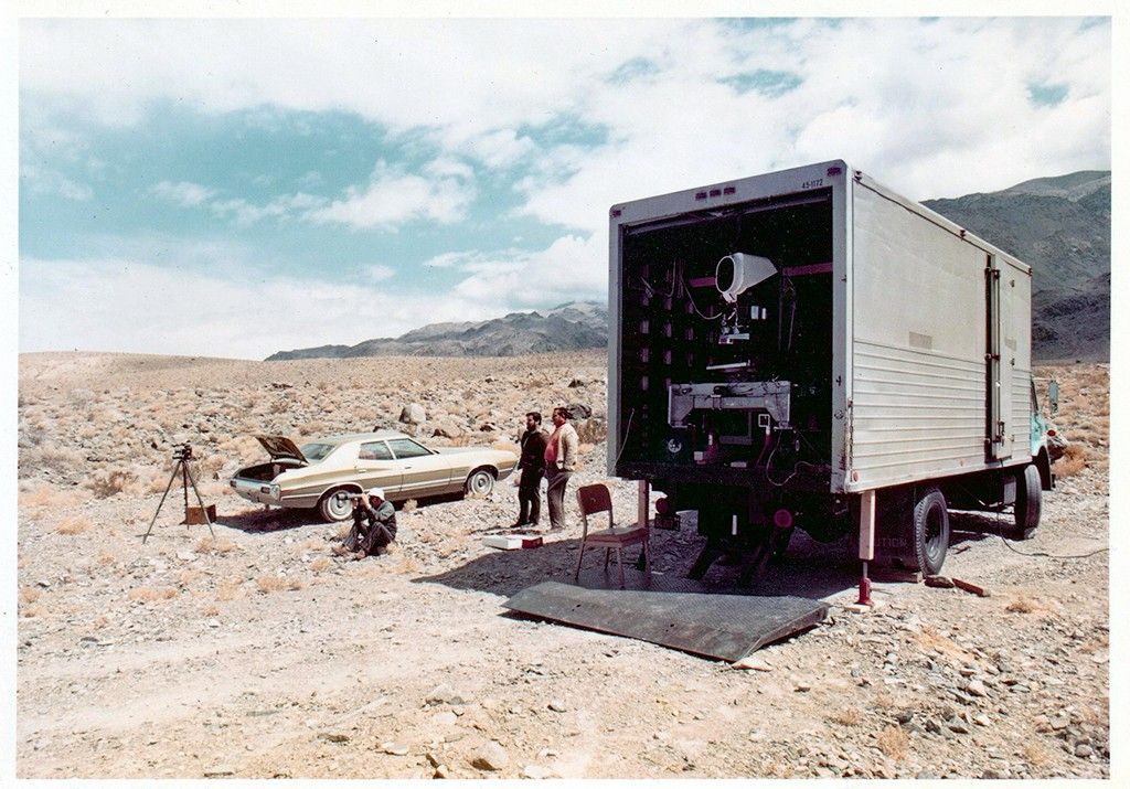 The Landsat 1 MSS engineering model on the back of a truck with three people, and a car in background.
