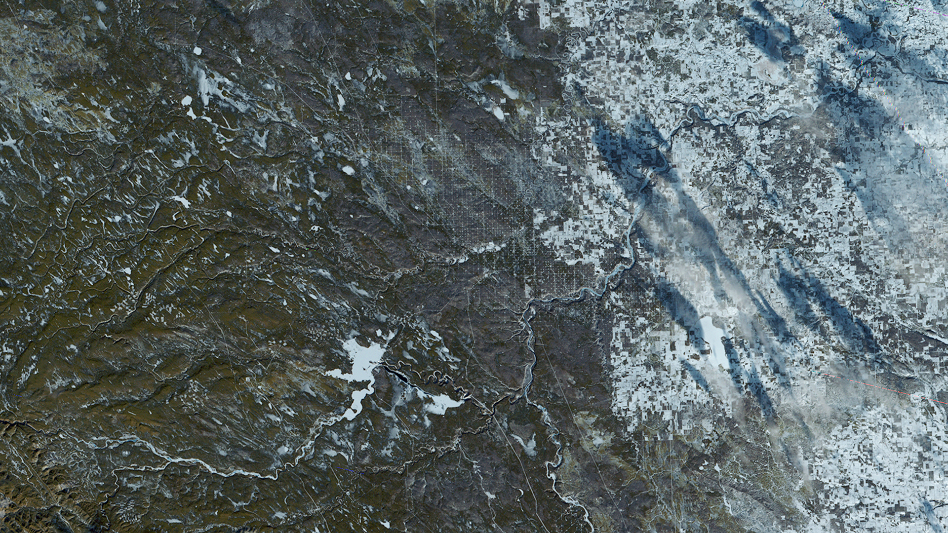 A satellite image of an area along the Canadian Highway 22, also known as the cowboy trail. The are in this image is greenish brown surrounded by the white blanket of snow to the north.